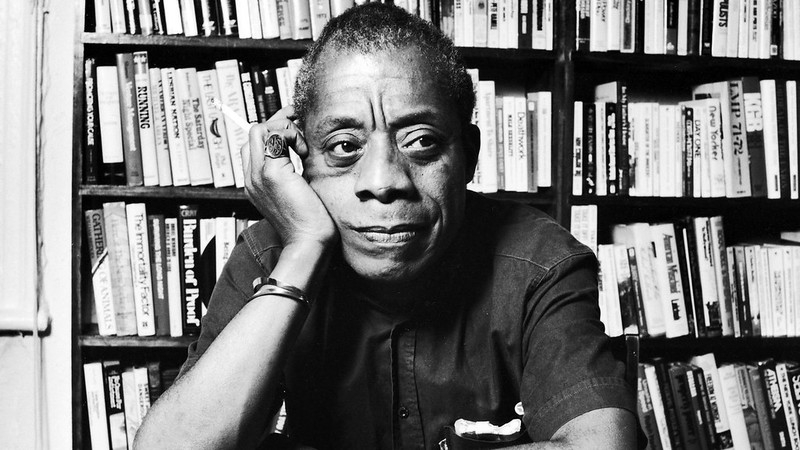 James Baldwin in front of bookshelf