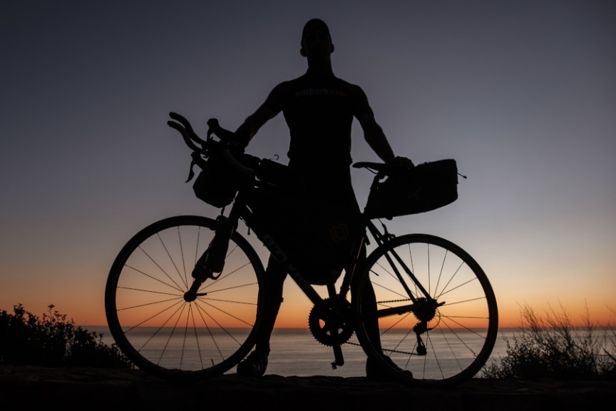 Silhouette of man with bike on coastal road