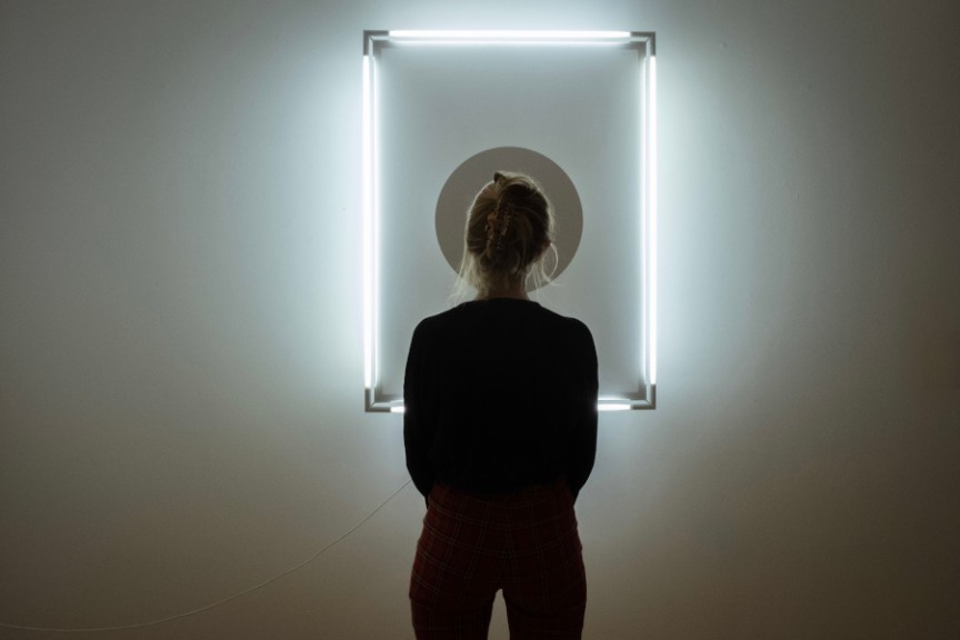 woman facing away from camera in front of mounted light sculpture