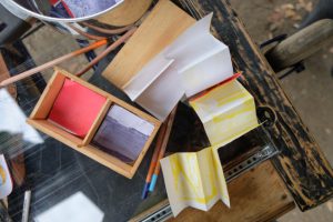 collection of coloured paper, paintbrushes and other art supplies on rustic wooden table