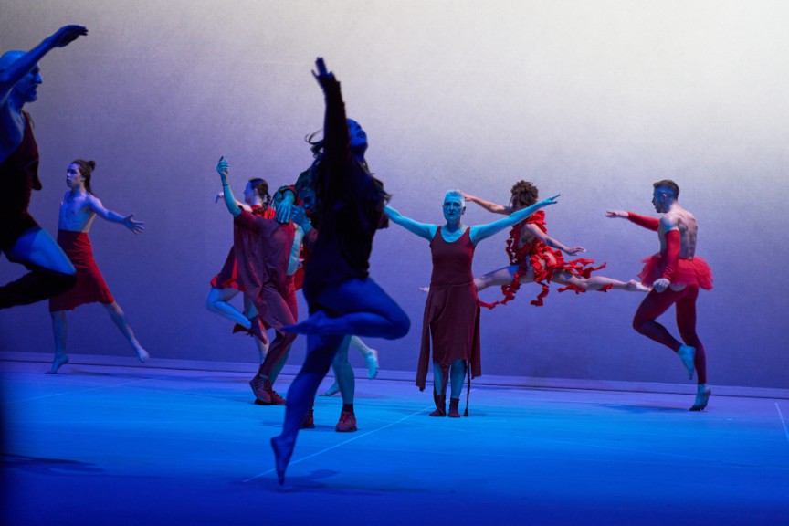 Dancers dressed in red, leaping in a circle, blue lit