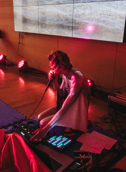 Female sitting behind mixing desk with microphone, lit in red