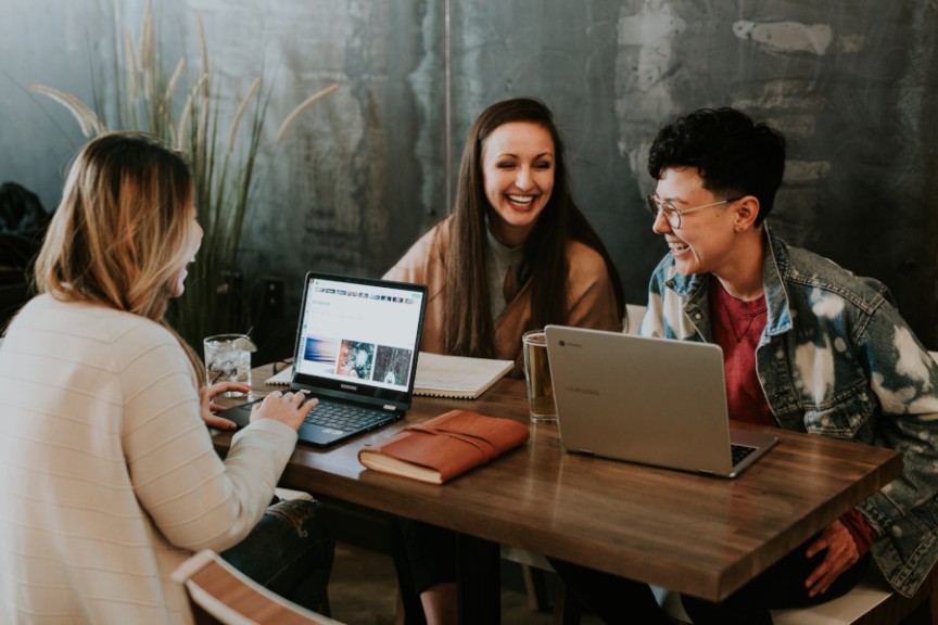 three laughing women seated at table with laptops