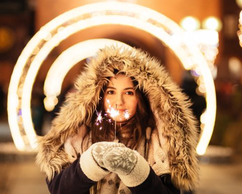 young woman facing camera in furry hood with sparkler