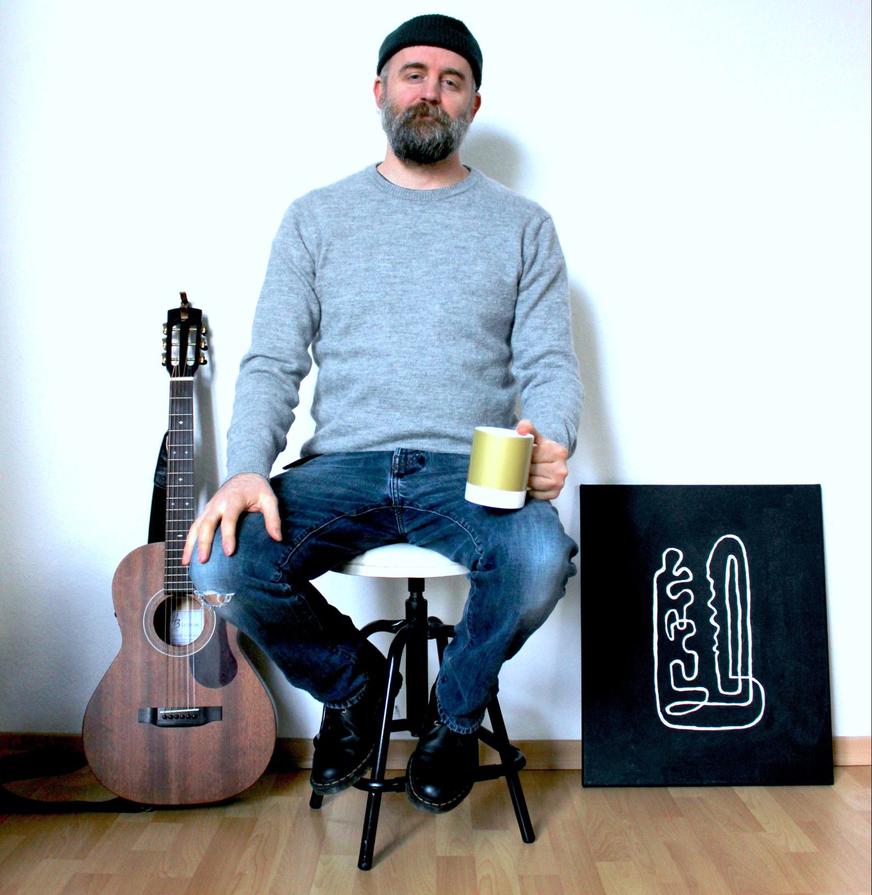 Portrait of Sammy H. Stephens, photo of a musician sitting in a chair holding a cup of coffee with a guitar nearby